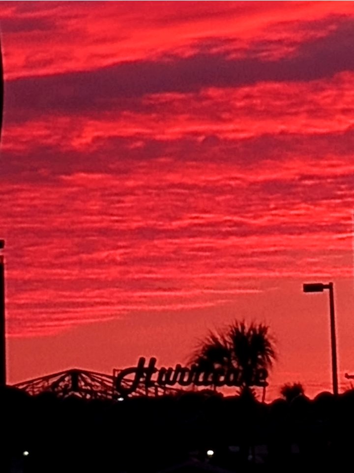 A blood-red sunset sky over the Myrtle Beach amusement park, with the Hurricane ride sign silhouetted in black below it
