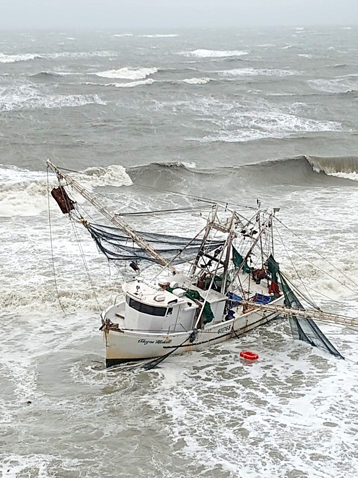 The shrimp boat Shayne Michelle in heavy gray surf during Hurricane Ian, her nets flying and a red life ring floating in the water beside her