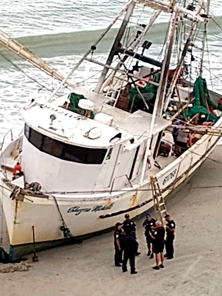 Officers standing on the sand at the bow of the beached Shayne Michelle, a ladder leaning against her hull